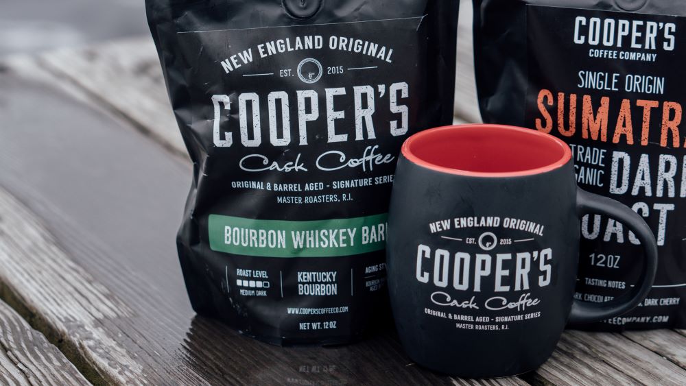 Bags of Cooper's Cask Coffees including whiskey barrel aged coffee next to a coffee cup representing great whiskey gifts for dad