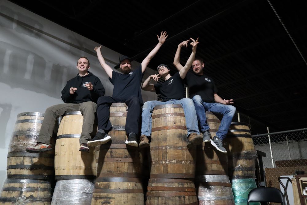 A group of guys sitting on whiskey barrels which will become great whiskey gifts for dad