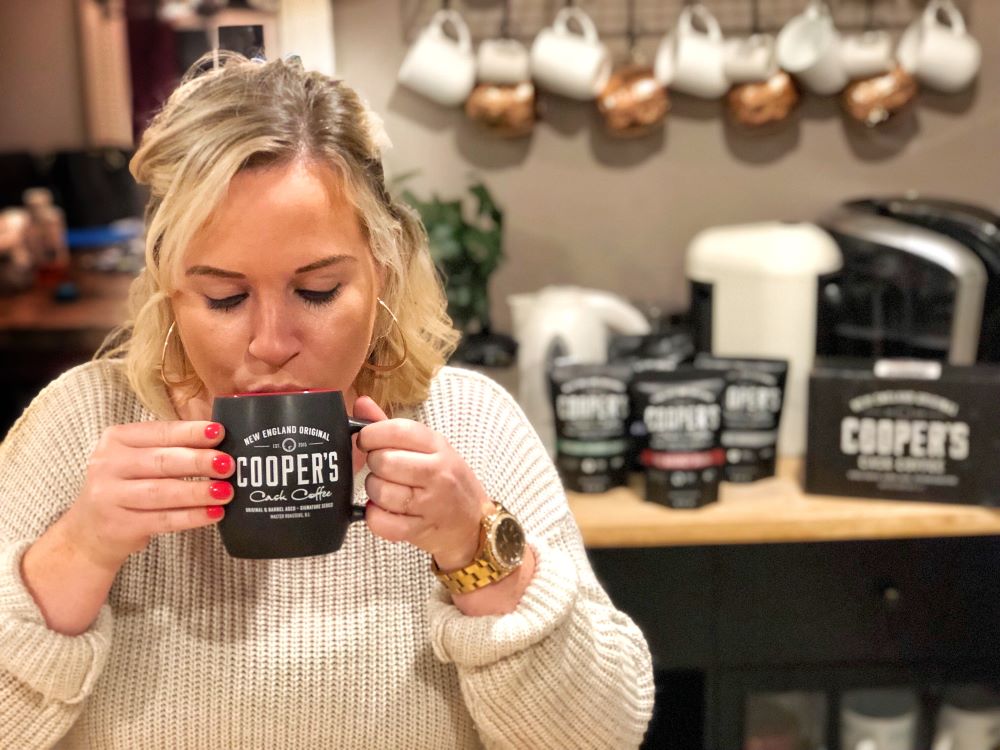 A lovely young woman drinking a hot cup of Cooper's Cask Coffee barrel aged coffee.