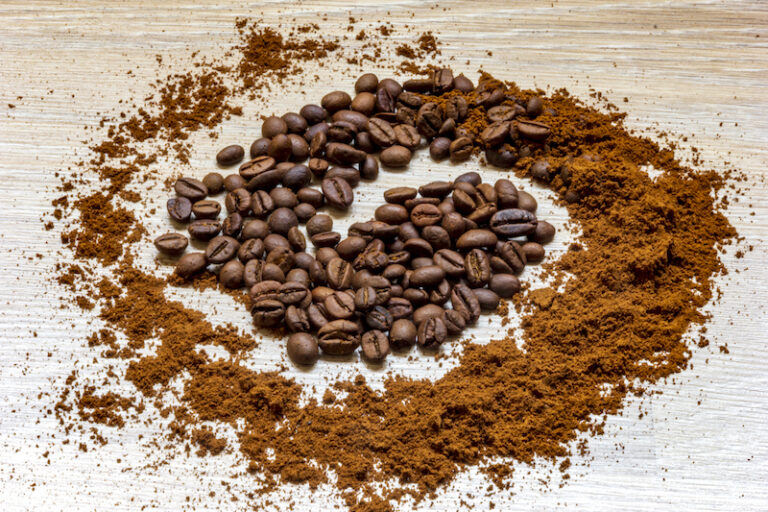 A swirl of coffee beans and ground coffee on a wood surface showing All You Need to Know About Whole Bean vs Ground Coffee