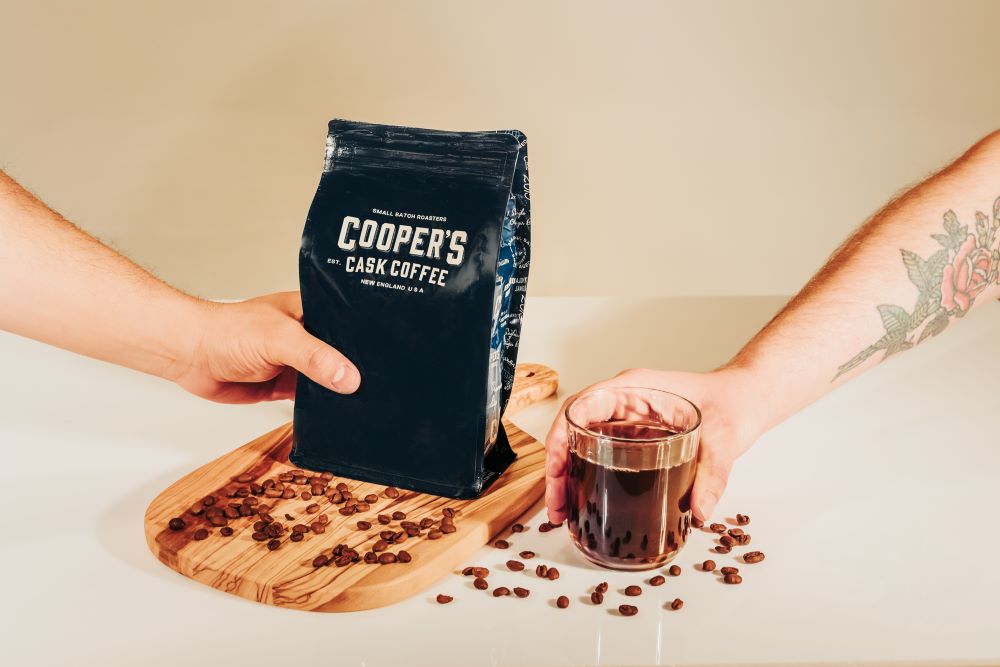 a bag of unroasted coffee and a cup of coffee with opposing hands to show how long does coffee last