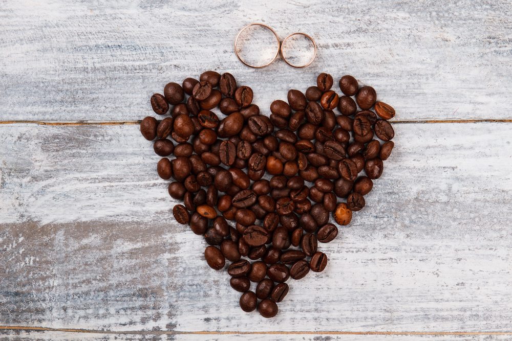 wedding rings on a board above coffee beans in shape of heart to hint at great coffee bridal party gifts