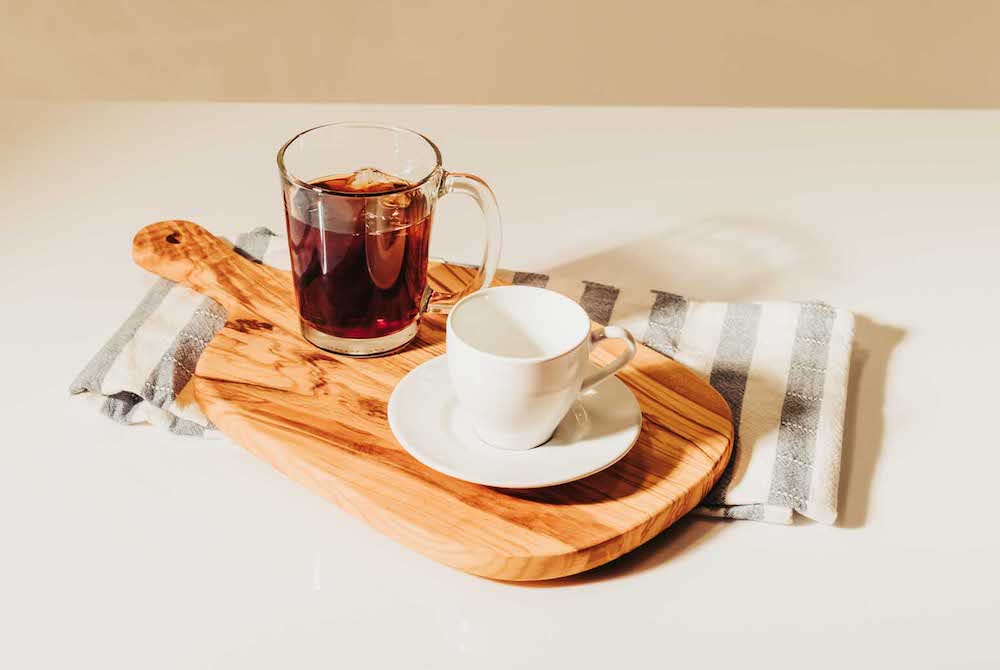 Two cups of bourbon coffee and a biscottie sitting on a cutting board to represent naturally flavored coffee