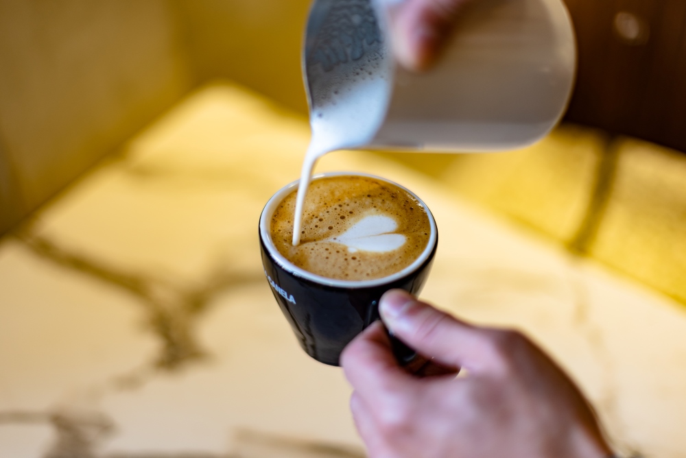 a hand holding a cup of espresso while the other pours milk into it showing the Difference Between Espresso Roast and Regular Roast