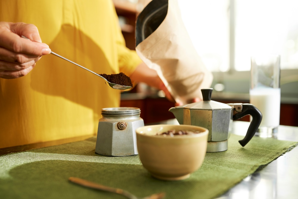 closeup of woman in kitchen showing how to make an espresso using a moka pot